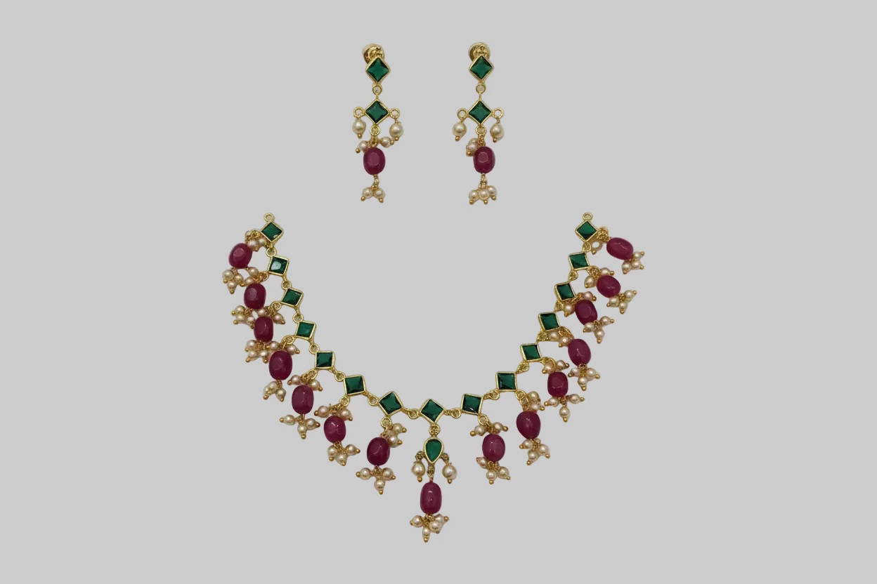 Jewelry set with necklace and earrings featuring red and green gemstones on a white surface.
