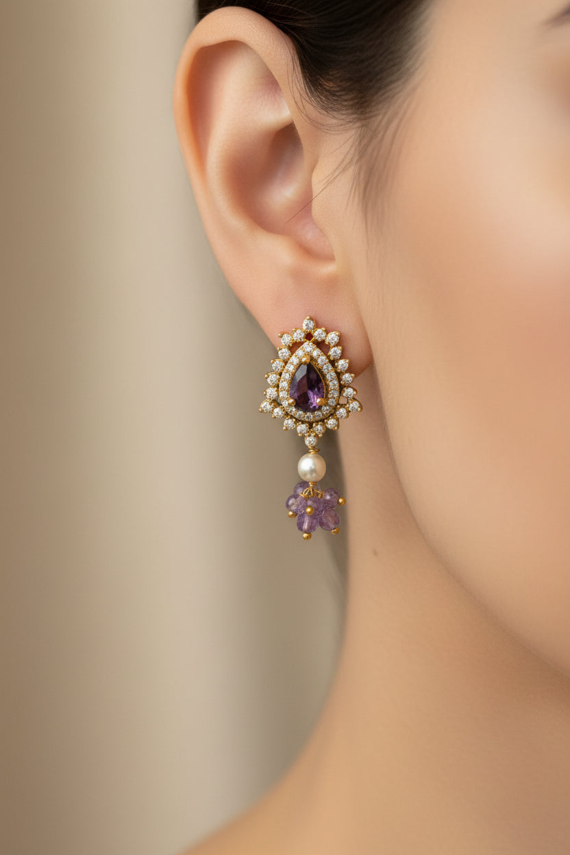 Close-up of an ear wearing a decorative earring with purple gemstones and pearls against a neutral background.
